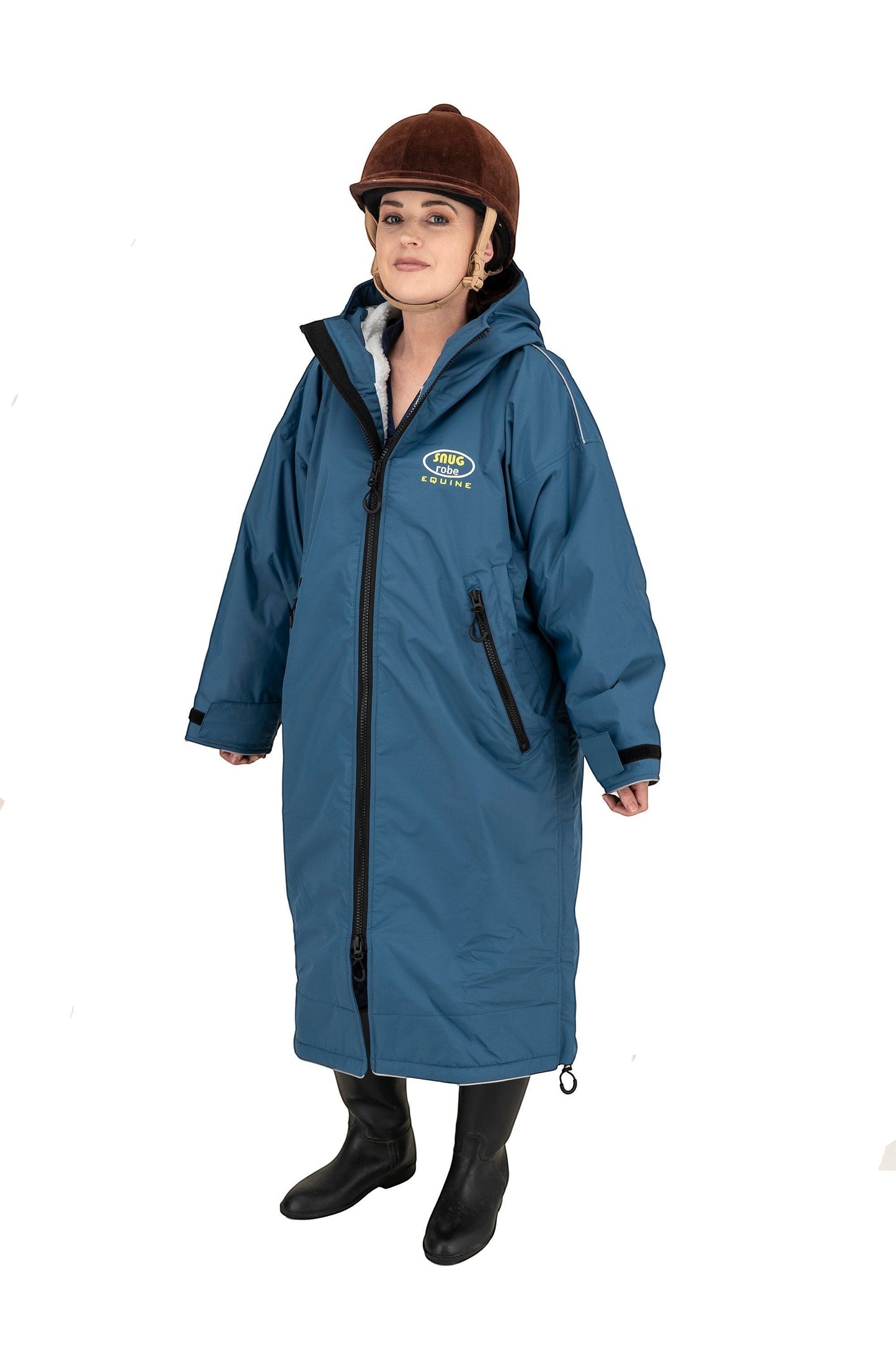 Snugrobes Equine waterproof robe in teal blue with fleece lining, hood, and reflective piping. Model wears riding helmet and boots.